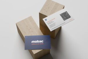 Visitenkarten von mobac GmbH, präsentiert auf Holzblöcken. Die Karte zeigt den Namen Florian Schiffer, Geschäftsführer, sowie Kontaktdaten und einen QR-Code.