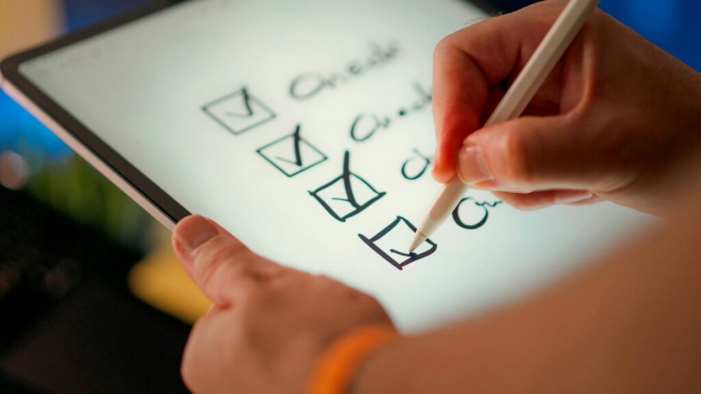 Eine Hand, die mit einem Stylus auf einem Tablet eine Checkliste abarbeitet, wobei mehrere Kästchen bereits markiert sind.