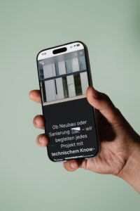 Hand, die ein Smartphone hält, zeigt eine Website über Neubau und Sanierung mit technischem Know-how.