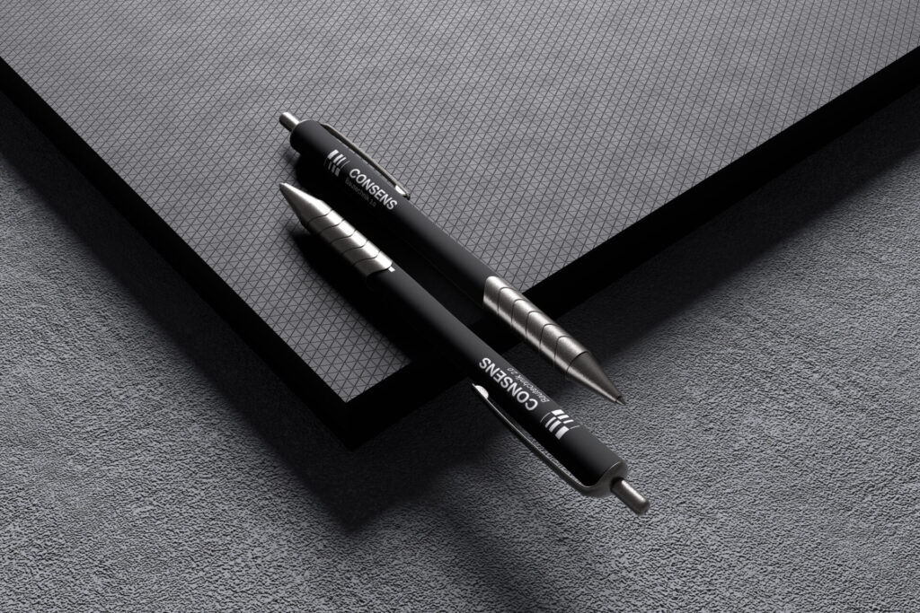 Zwei schwarze Kugelschreiber auf einem strukturierten, dunklen Untergrund. Die Stifte sind mit der Marke "CONSENS" versehen und liegen auf einer matten, geometrisch gemusterten Fläche.