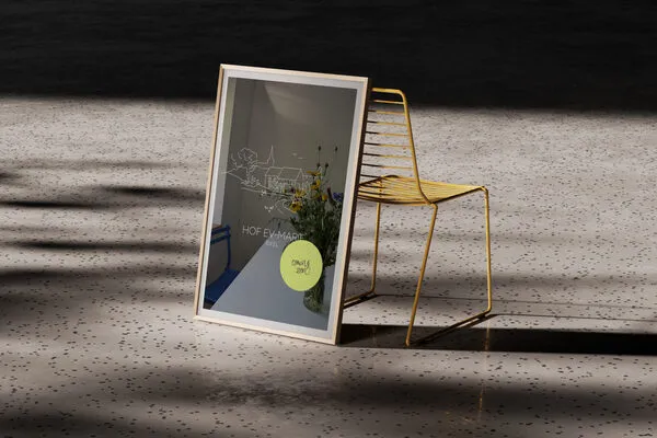 Ein moderner Raum mit einem goldenen Stuhl und einem großen, rahmenlosen Spiegel, der eine Zeichnung und frische Blumen zeigt. Der Boden ist aus hellem Material mit kleinen schwarzen Punkten.