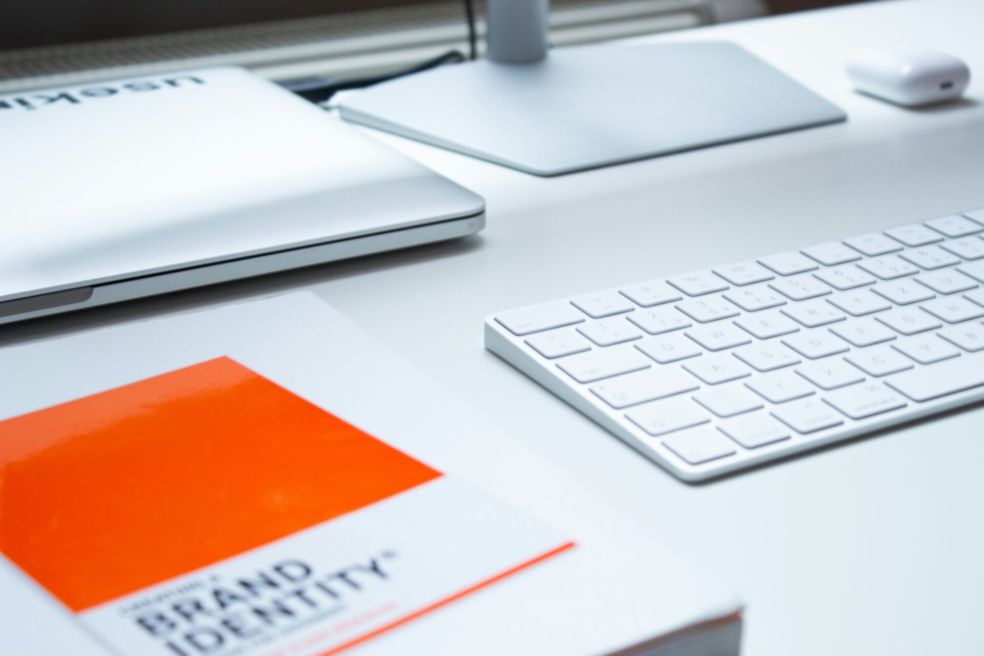 Schreibtisch mit einem Laptop, einer weißen Tastatur und einem Buch über Markenidentität, das eine orangefarbene Coverseite hat.