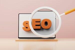 Nahaufnahme eines Laptops mit dem Fokus auf den orangefarbenen Buchstaben "SEO", umgeben von einer Lupe, vor einem sanften rosa Hintergrund.