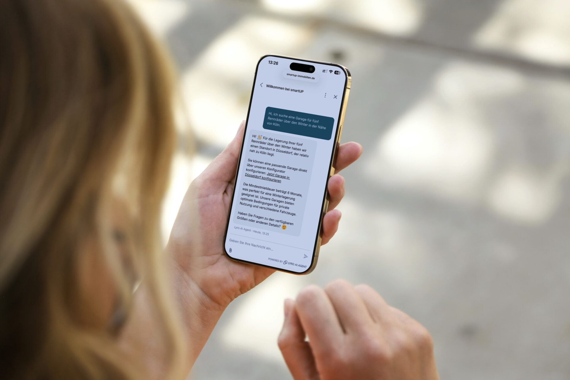 Eine Person hält ein Smartphone in der Hand, auf dem eine Chat-Nachricht von smartup angezeigt wird. Der Text bezieht sich auf die Suche nach einer Garage in der Nähe von Köln und bietet Unterstützung bei der Vermittlung geeigneter Optionen.