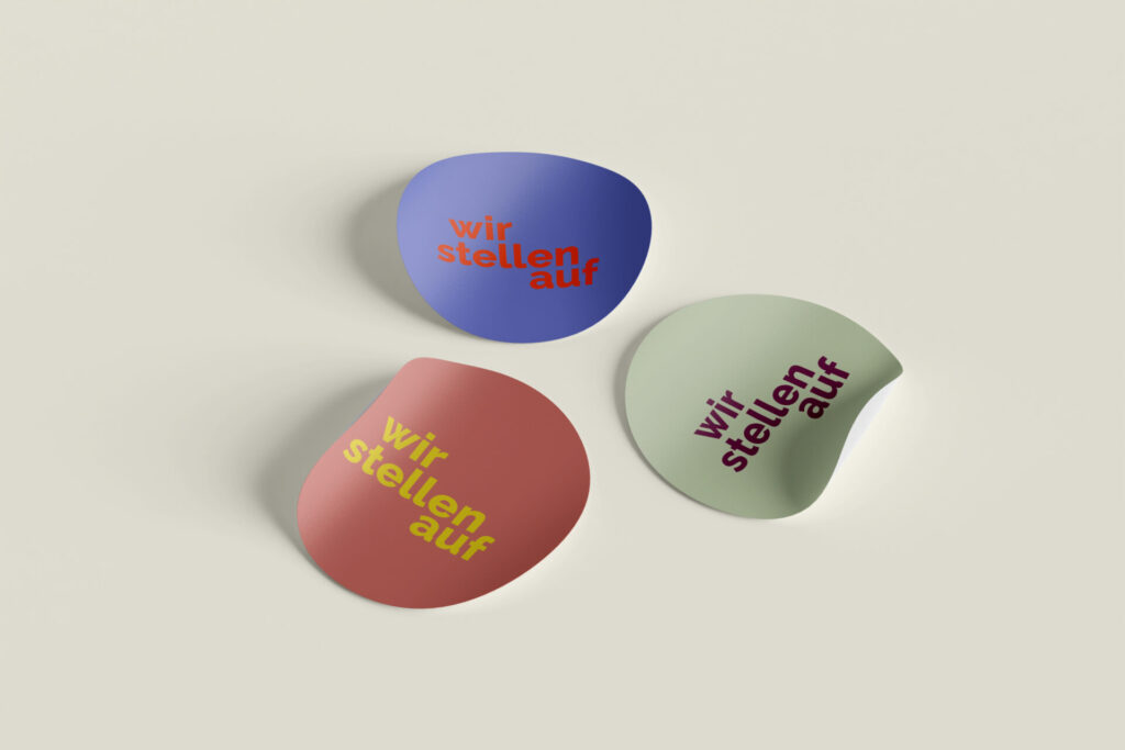 Bunte Aufkleber in verschiedenen Formen mit den Aufschriften „wir stehen auf“ in lila, rot und grün auf einem neutralen Hintergrund. Ideal für kreative Projekte oder zur Verschönerung von Notizen.