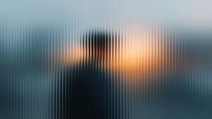 Verschwommene Silhouette einer Person hinter strukturiertem Glas bei Sonnenuntergang. Die warmen Farben des Himmels sind sichtbar, während die Linien des Glases eine interessante Textur schaffen.