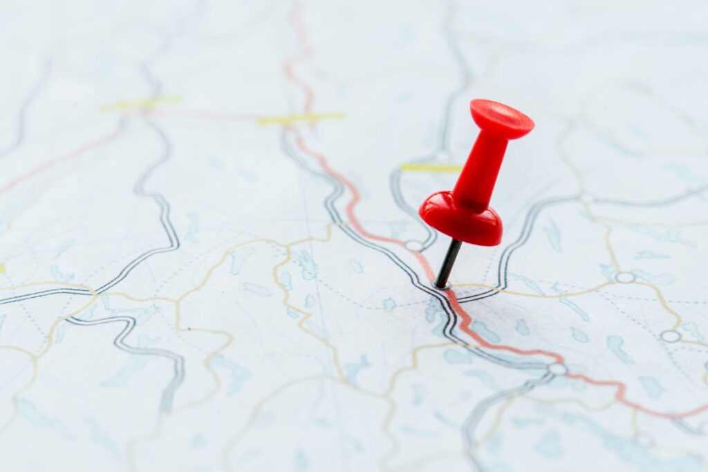 Roter Stecknadel auf einer detaillierten Landkarte, die verschiedene Straßen und Gewässer zeigt, zur Veranschaulichung von Reiserouten und Navigation.
