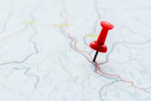 Roter Stecknadel auf einer detaillierten Landkarte, die verschiedene Straßen und Gewässer zeigt, zur Veranschaulichung von Reiserouten und Navigation.