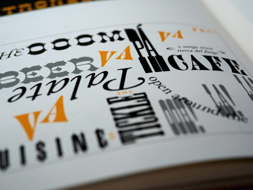 Bunte Typografie auf einer Buchseite, die verschiedene Schriftarten und -stile zeigt. Die Wörter "Cuisine", "Café" und "Beer" sind hervorgehoben, um die kreative Gestaltung und Vielfalt der Schriftarten zu präsentieren.