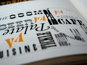 Bunte Typografie auf einer Buchseite, die verschiedene Schriftarten und -stile zeigt. Die Wörter "Cuisine", "Café" und "Beer" sind hervorgehoben, um die kreative Gestaltung und Vielfalt der Schriftarten zu präsentieren.