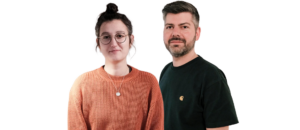 Portrait eines Mannes und einer Frau vor schwarzem Hintergrund. Die Frau trägt einen orangefarbenen Pullover und eine Kette, während der Mann ein schwarzes T-Shirt mit Logo trägt. Beide schauen freundlich in die Kamera.