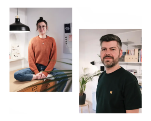 Zwei Personen in einem modernen Arbeitsumfeld: Eine Frau mit Brille und orangefarbenem Pullover sitzt auf einem Tisch, während ein Mann mit Bart und schwarzem T-Shirt im Hintergrund steht. Beide wirken freundlich und professionell.